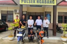 Unit Reskrim Polsek Ngabang bersama terduga pelaku berjongkok di belakang barang bukti dua sepeda motor di halaman Polsek Ngabang. Yamaha Jupiter berada di sisi kiri, sedangkan Suzuki Satria berada di sisi kanan.